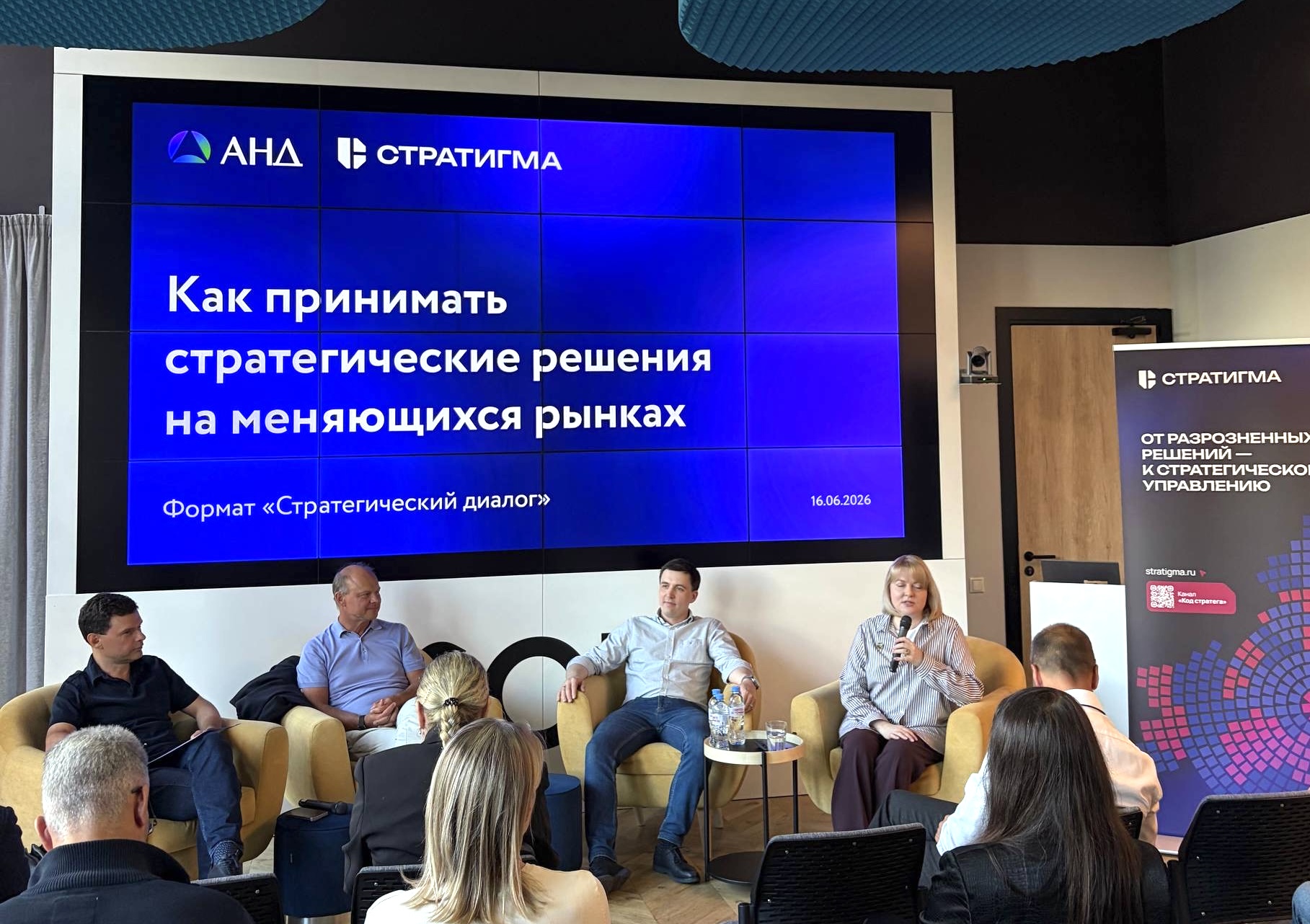Панель «Стратегический диалог»: на экране тема «Как принимать стратегические решения на меняющихся рынках», логотипы АНД и «Стратигмы», на сцене три спикера и модератор